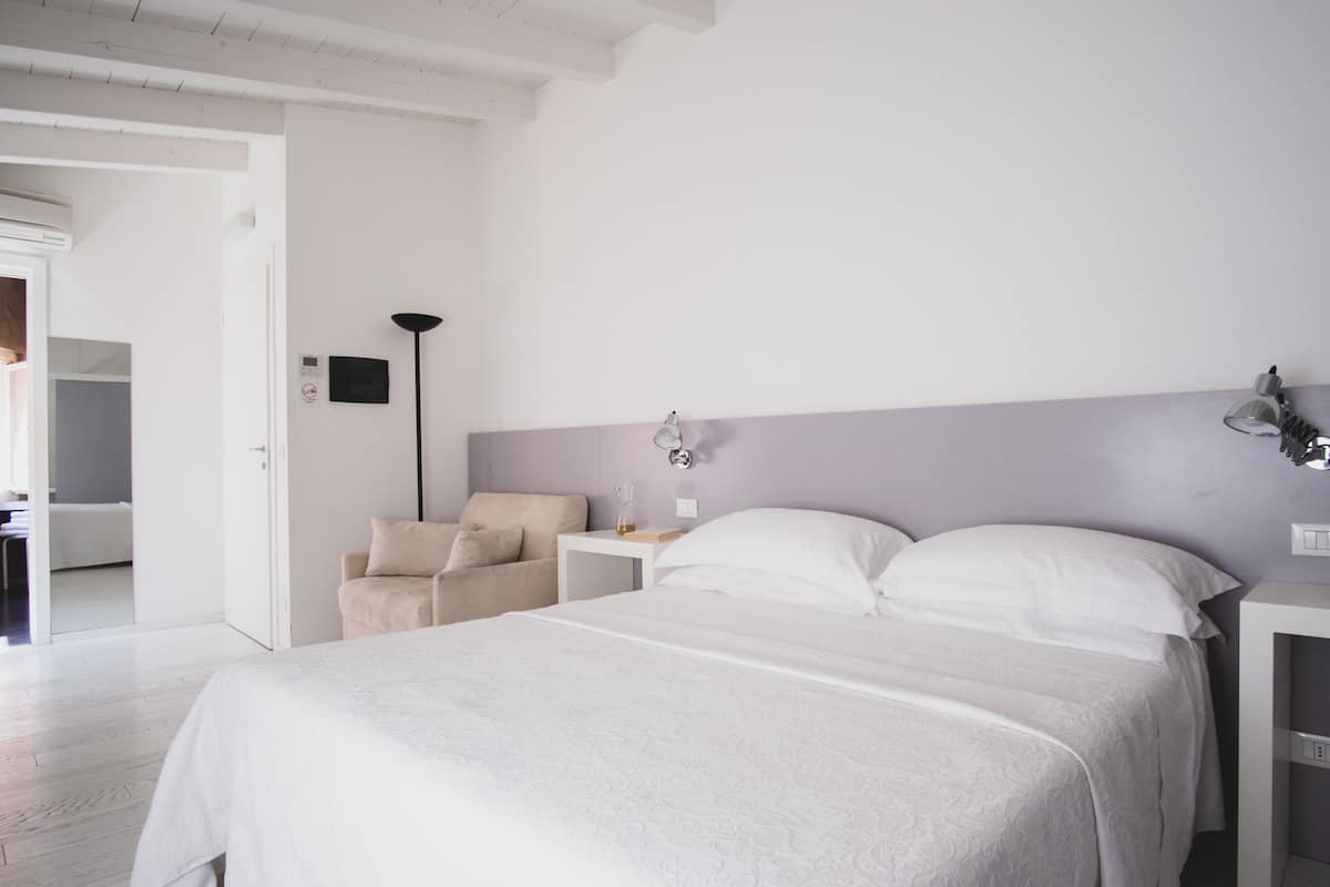 A bedroom with a large bed, a bedside table, a chair, and a lamp.