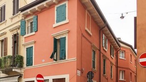 Un edificio de varios pisos con fachada roja, contraventanas verdes y un letrero de prohibido el acceso.