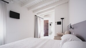 Habitación de hotel moderna con una cama grande, un televisor de pantalla plana, una lámpara de noche y vistas al pasillo.