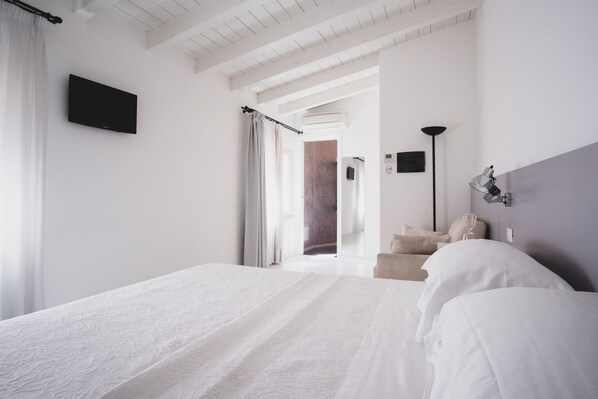 A modern hotel room with a large bed, a flat-screen TV, a bedside lamp, and a view of the hallway.