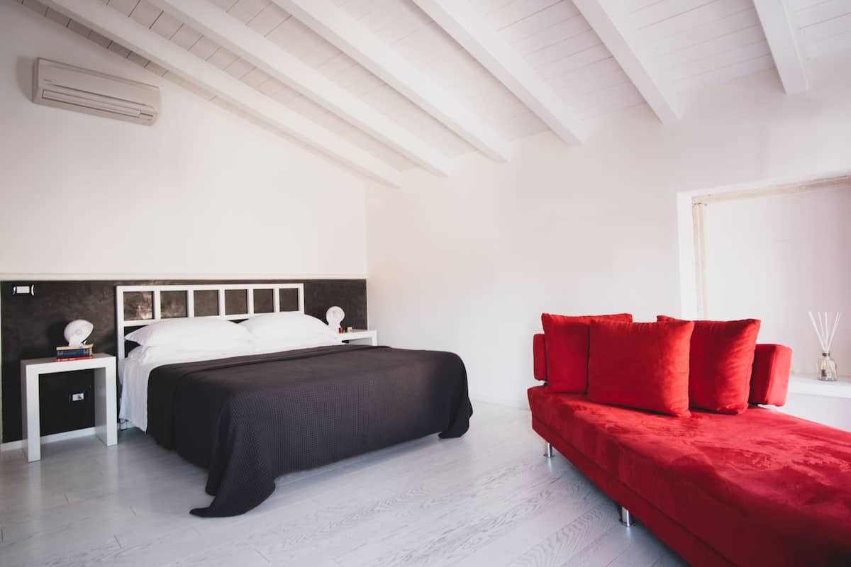 A modern bedroom with a bed, bedside tables, and a red sofa.