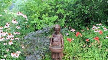A garden statue of a girl holding a basket amidst various flowers and greenery.