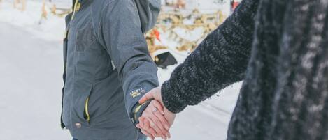 Two people holding hands in a snowy outdoor setting with bare trees and string lights in the background.