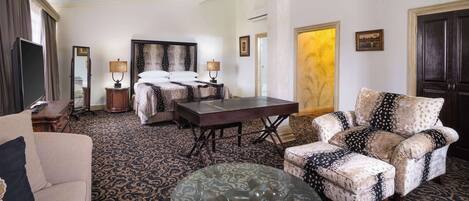 A hotel room with a bed, a sofa, a glass coffee table, a chair, and a TV.