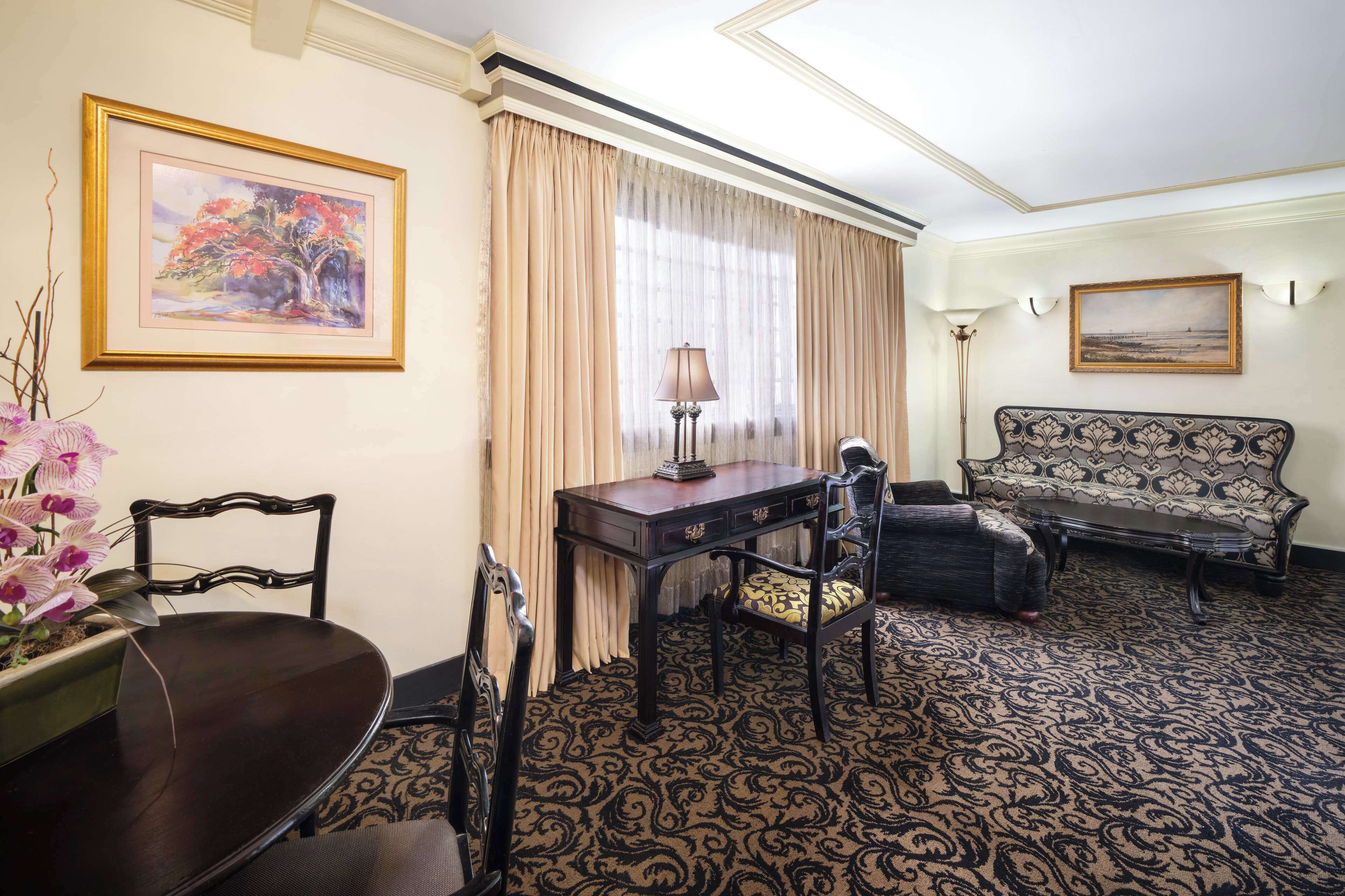A room with a dining table, chairs, a sofa, and a lamp.