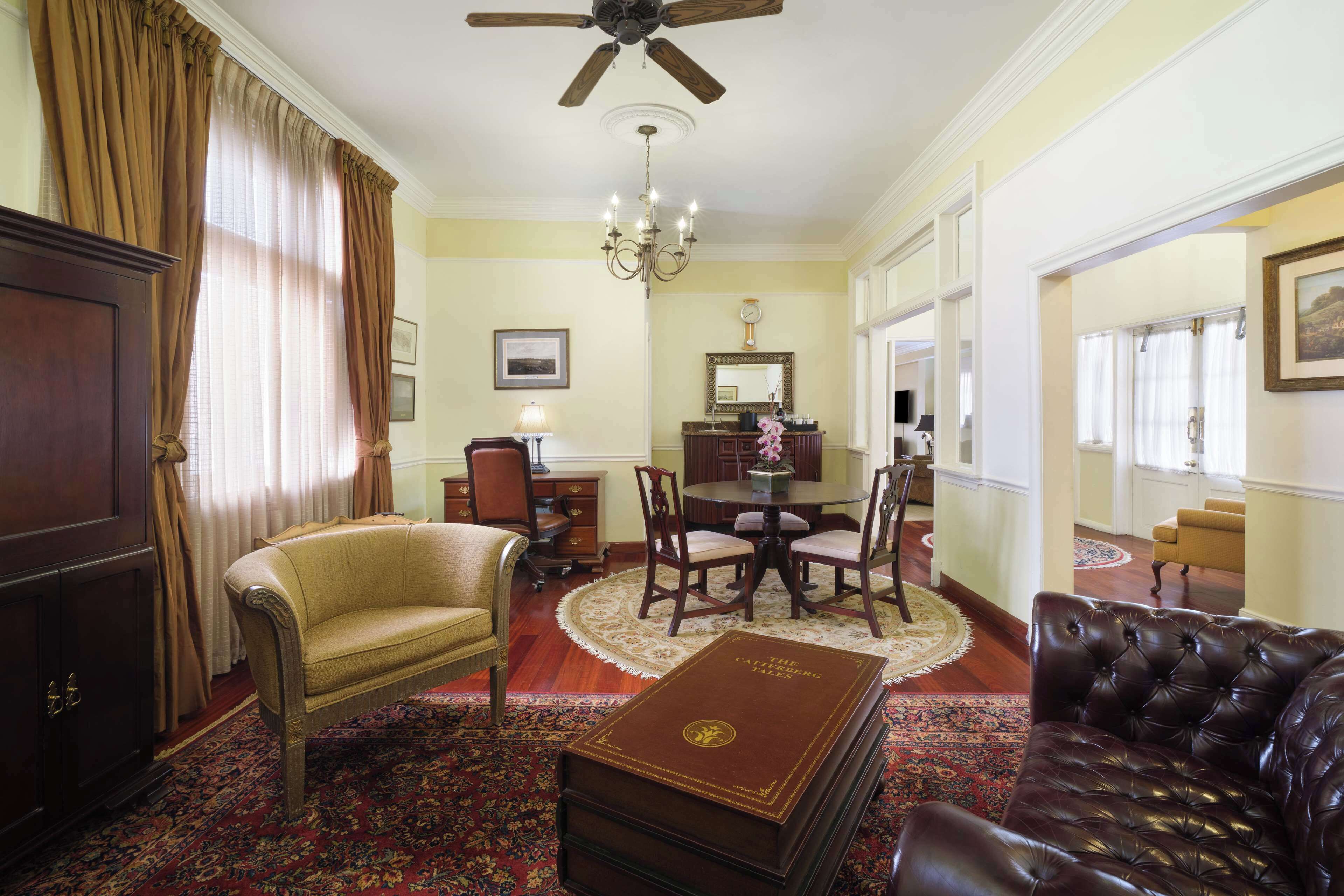 A traditional room with a sofa, a leather armchair, a dining table with chairs, a chandelier, and a large book on a table.
