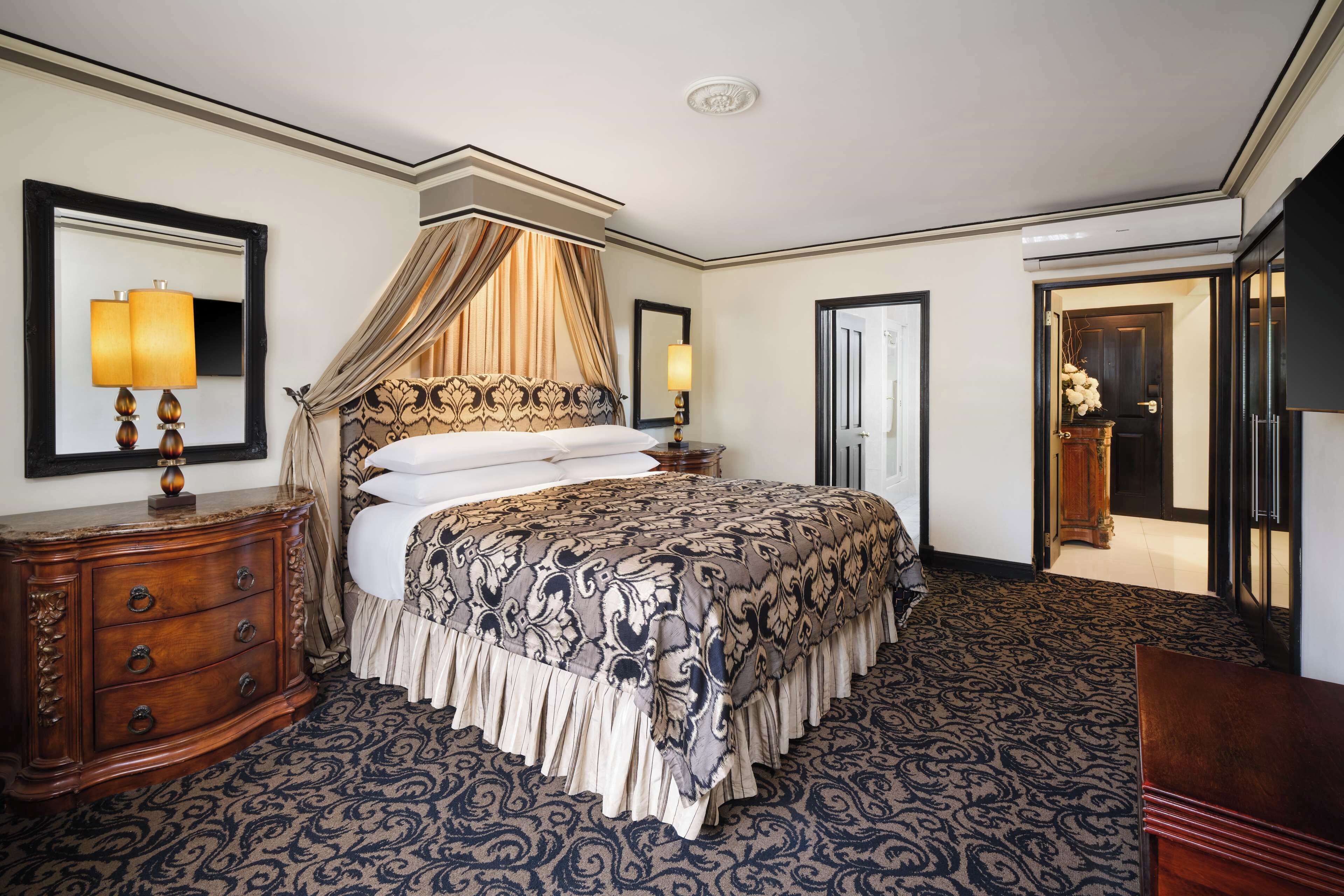A spacious bedroom with a large bed, a nightstand, a dresser, and a mirror.