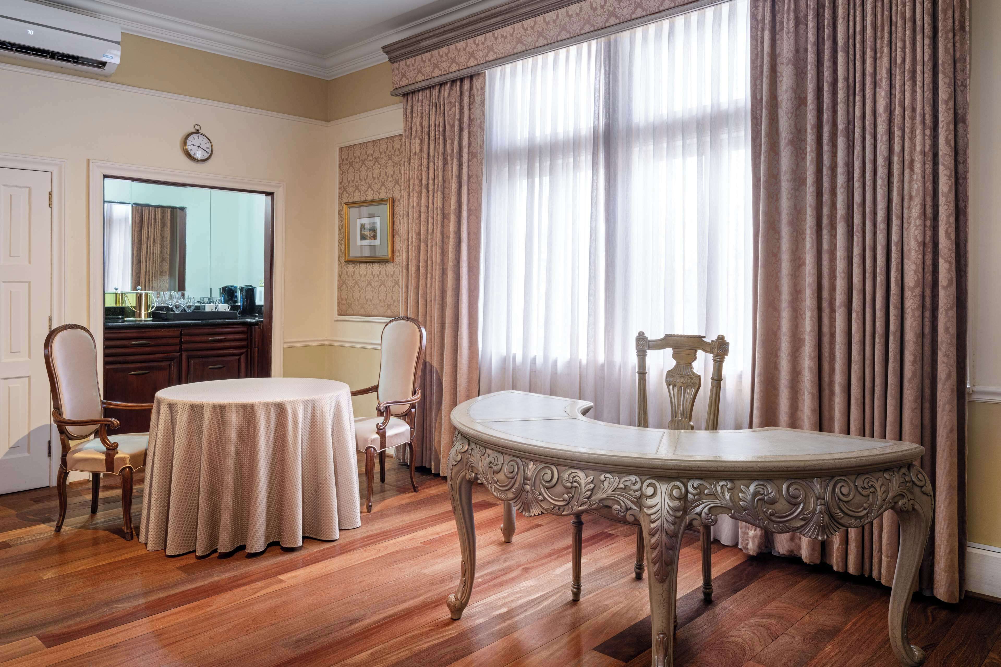 Un coin repas avec une table ronde et des chaises, un grand miroir et une vue à travers des rideaux légers.