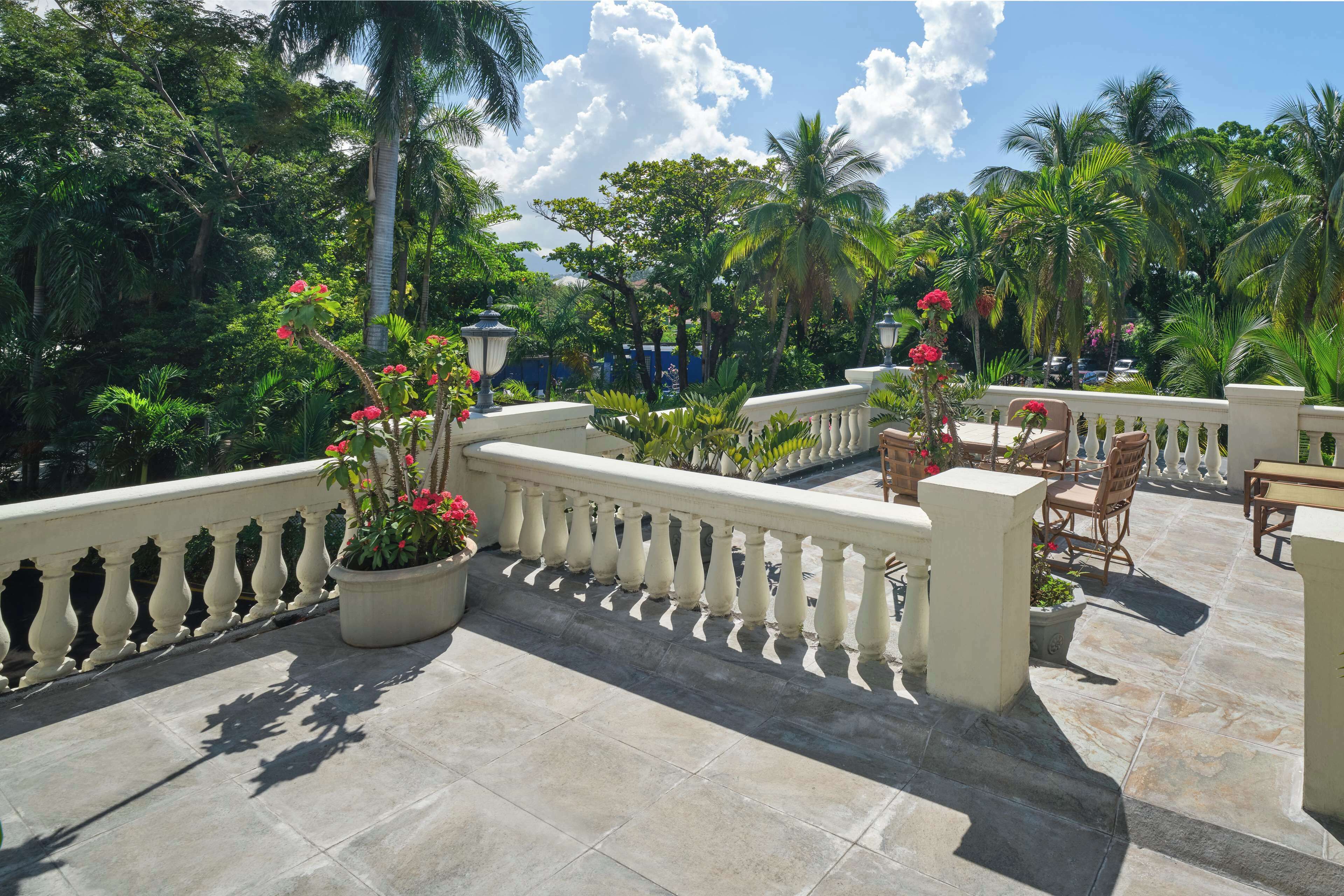 A terrace with a stone balustrade, potted plants, and outdoor furniture.