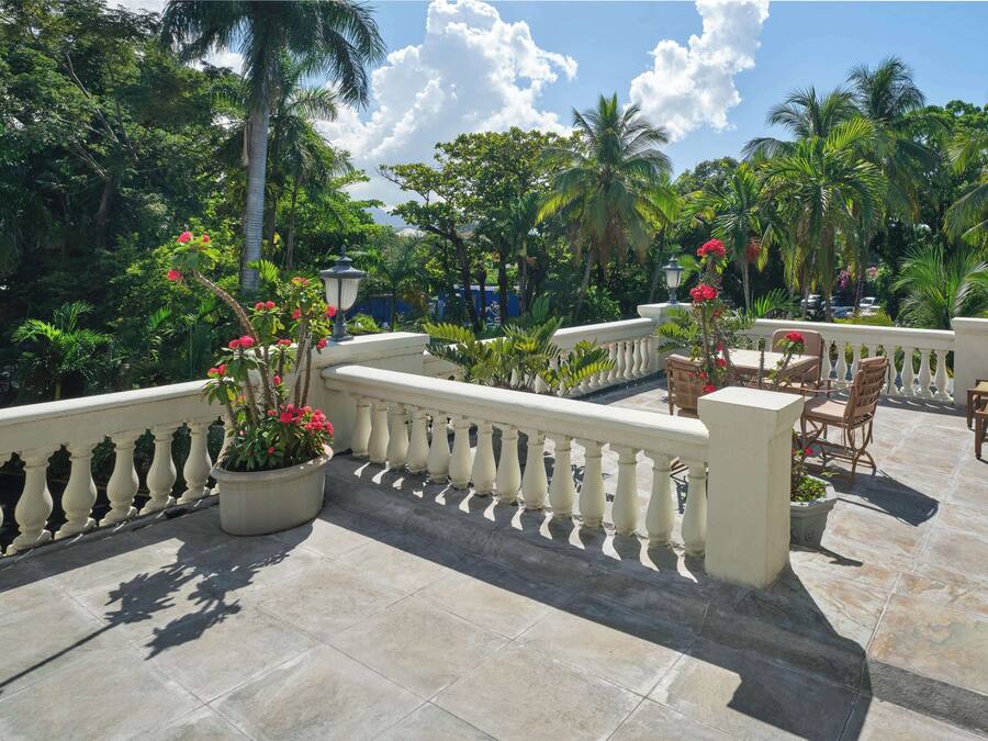 Una terraza con barandilla de piedra, macetas con plantas y mobiliario exterior.