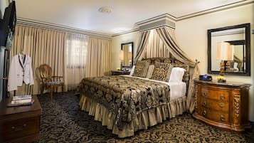 Une chambre d’hôtel avec un lit à baldaquin, une commode en bois, une chaise et un téléviseur.
