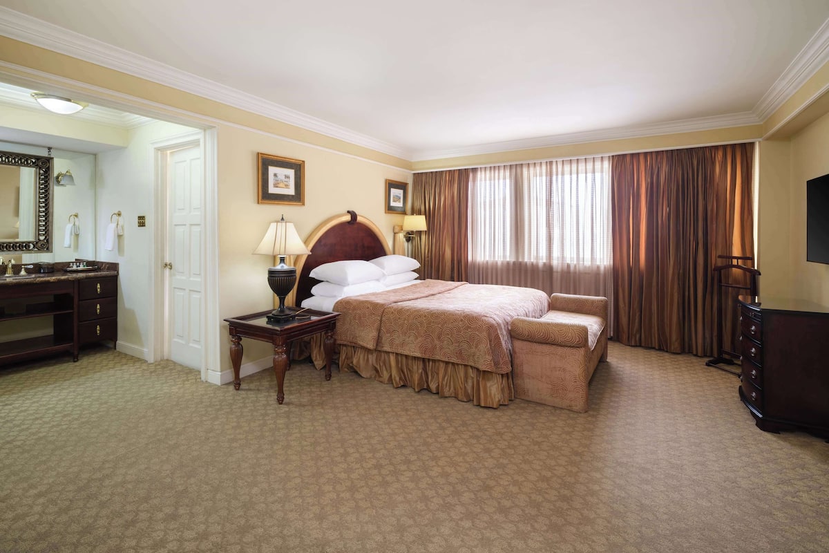 Ein Hotelzimmer mit Bett, Schreibtisch, Stuhl, Kommode und einem großen Spiegel.
