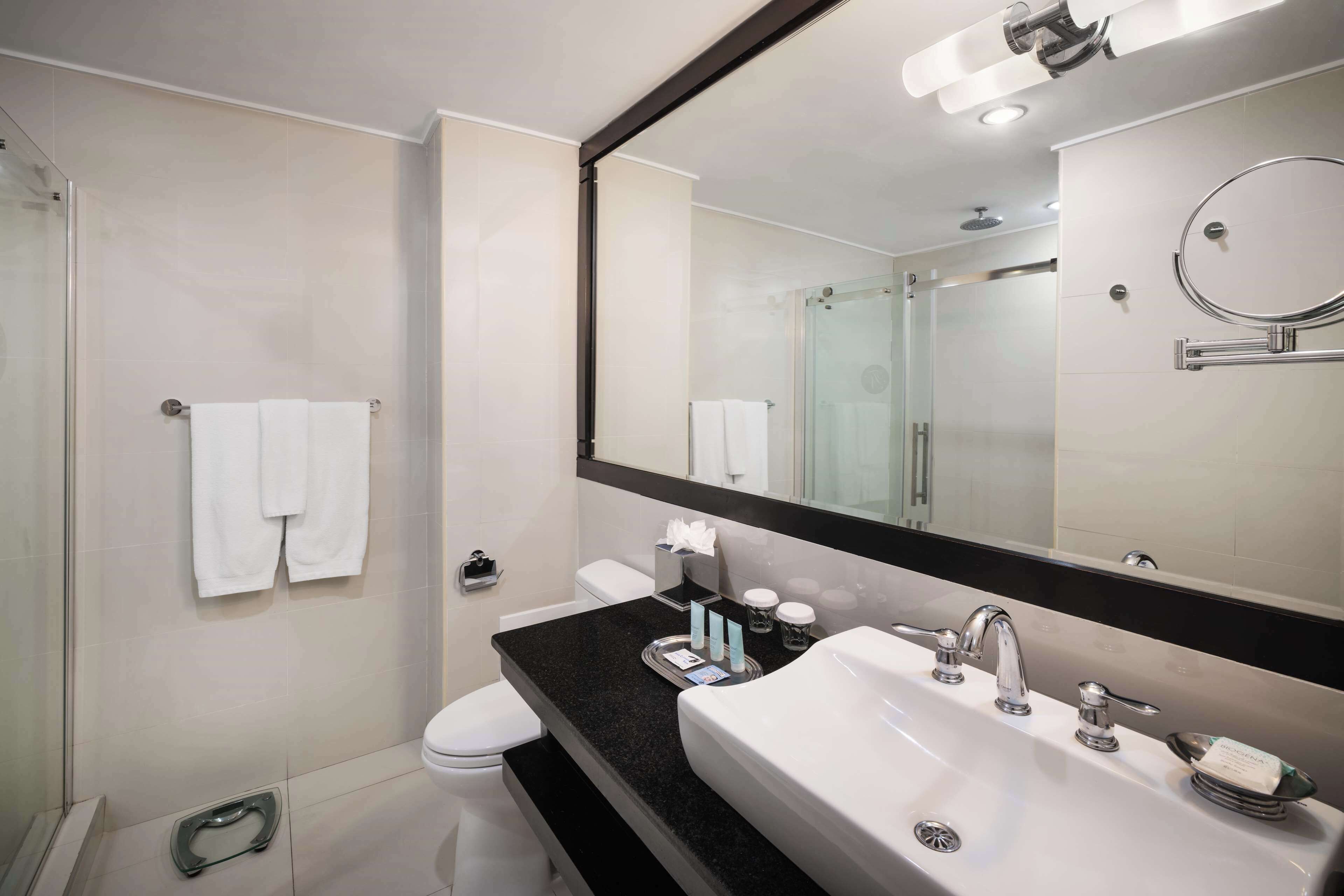 Un baño moderno con un espejo grande, una encimera negra, un lavabo blanco y una cabina de ducha con paredes de cristal.