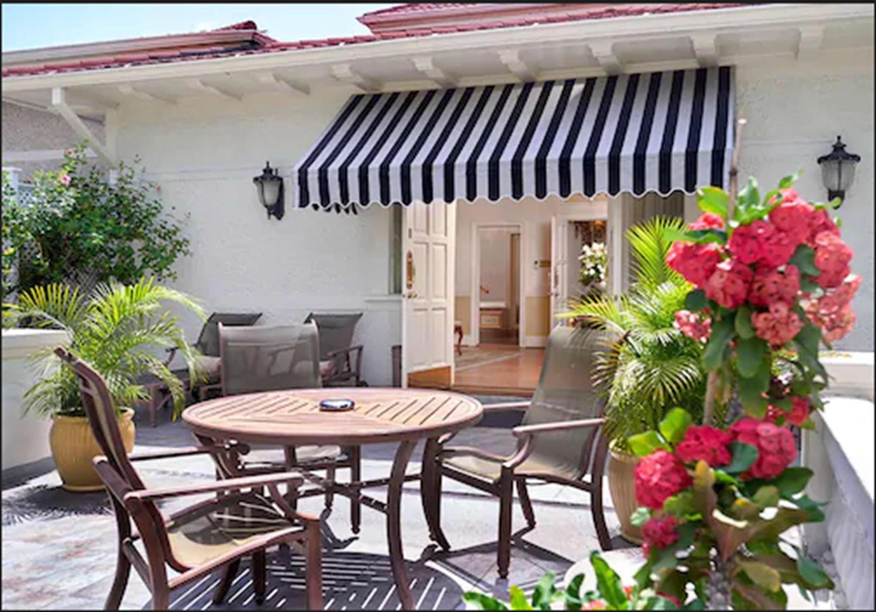An outdoor patio with a round wooden table and chairs, a striped awning, and potted plants.