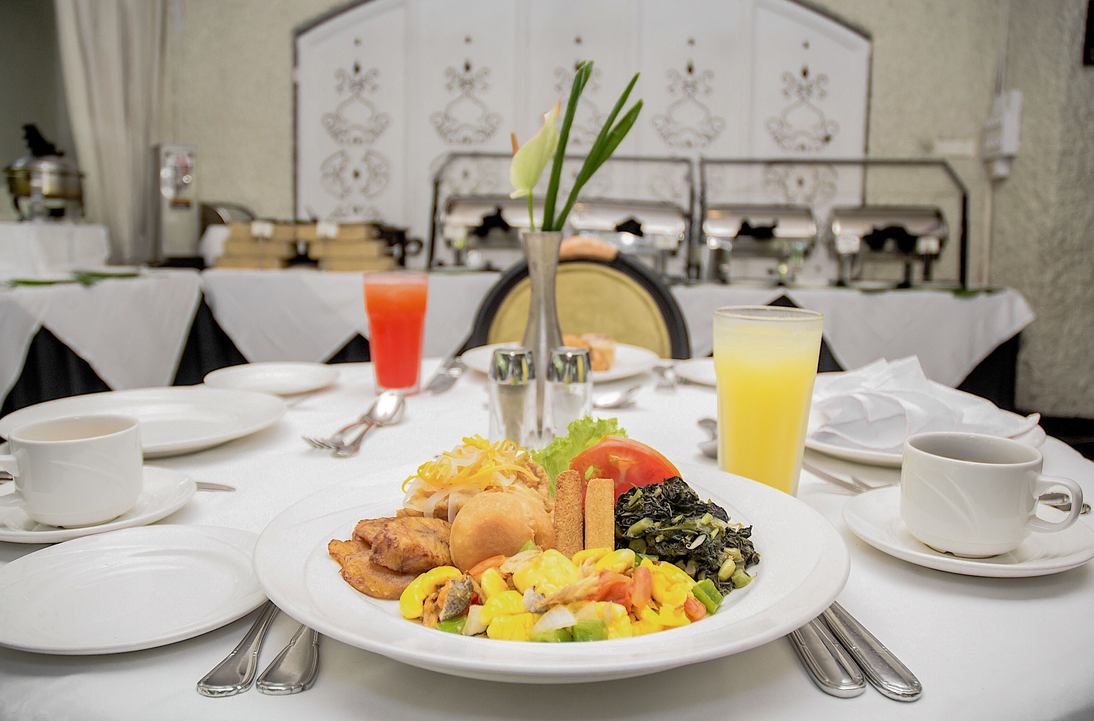 A breakfast setting with plates of food, cups, and a vase with flowers.