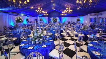 Un salón de banquetes con mesas redondas, manteles azules y sillas plateadas.
