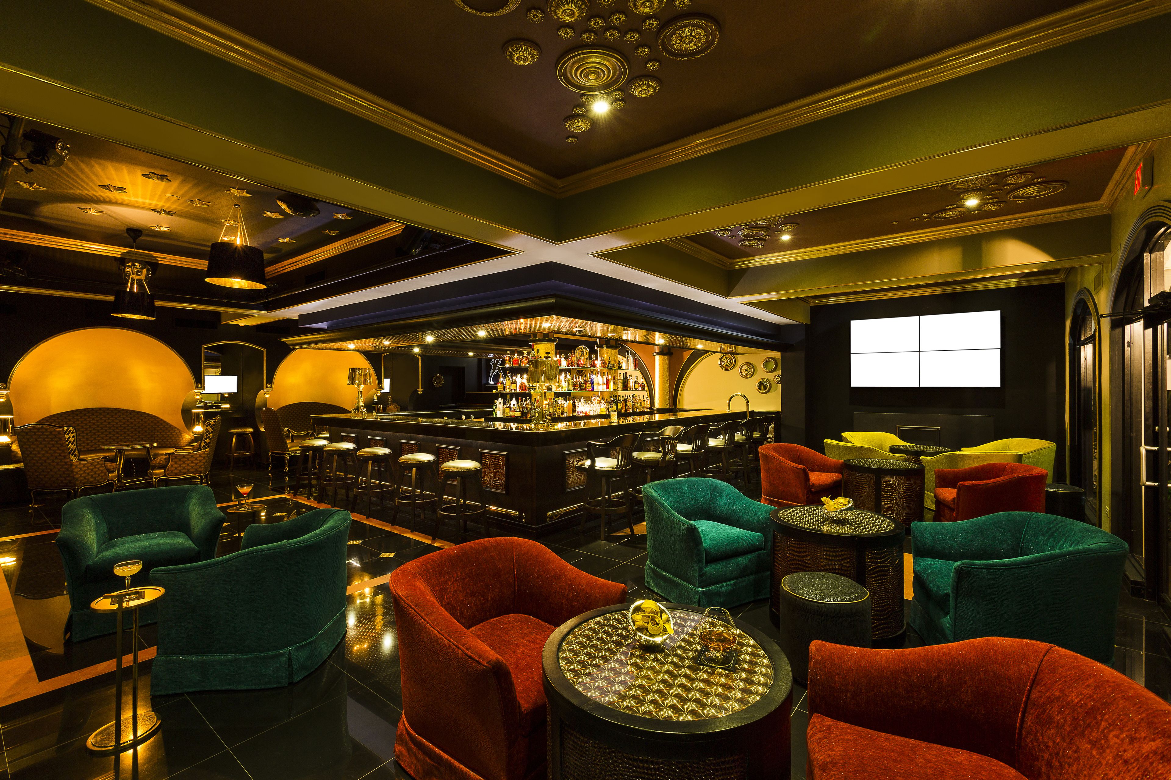 Een barruimte met verschillende zitmogelijkheden, waaronder rode en groene bekleden stoelen, en een bar met diverse flessen.