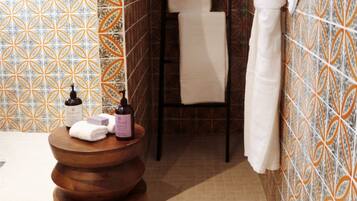 Un baño con baldosas estampadas, un taburete de madera, un perchero y una botella de loción.