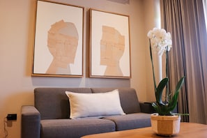 Un soggiorno con un divano grigio, due opere d'arte incorniciate al muro e un'orchidea in vaso su un tavolo di legno.