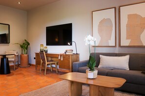 A modern living room with a sofa, a wooden coffee table, a desk with a chair, a potted plant, and artwork on the wall.