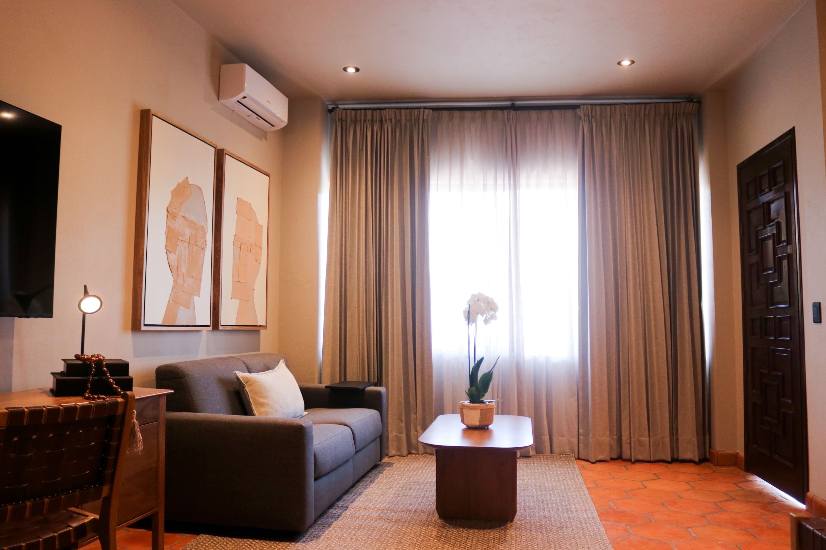 Una sala de estar con un sofá, una mesa de centro, un televisor y un ventanal con cortinas.