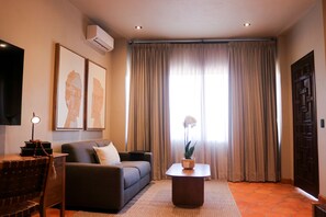 Una sala de estar con un sofá, una mesa de centro, un televisor y un ventanal con cortinas.