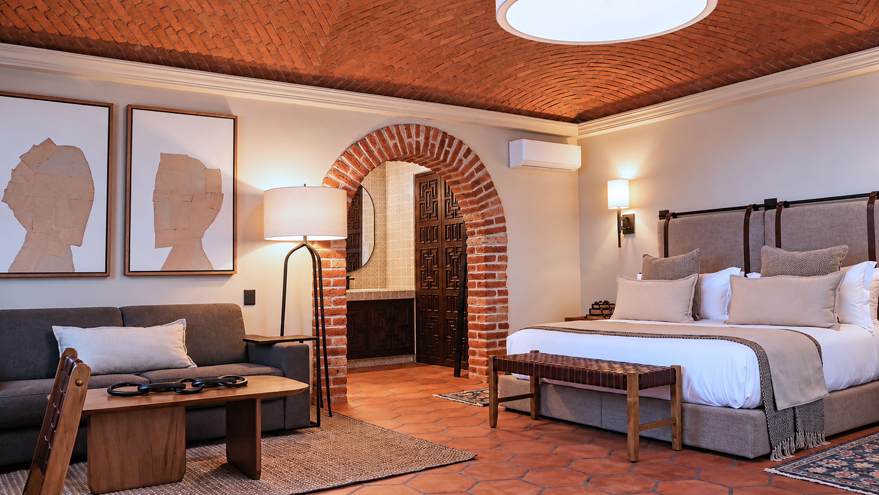 Habitación de hotel con chimenea de ladrillo, una cama con muchas almohadas, un sofá, una mesita de café y dos obras de arte enmarcadas.