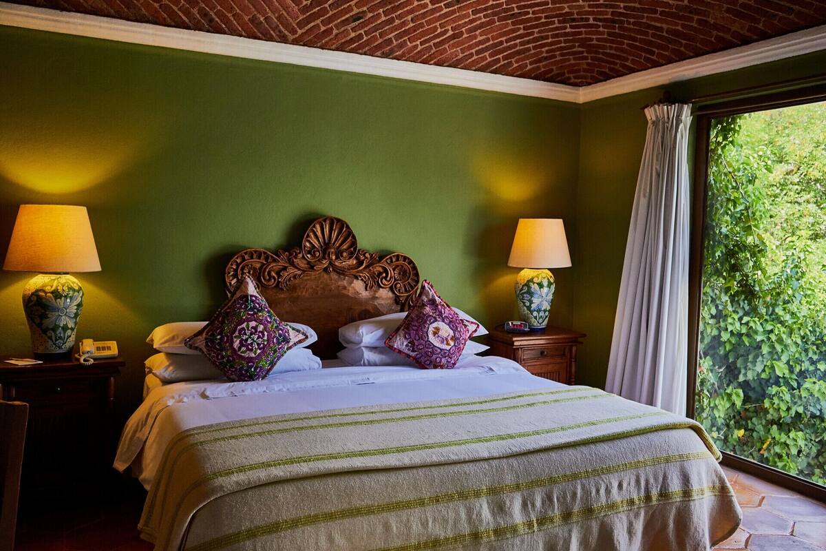 Una cama con una colcha verde a rayas, dos lámparas de noche y un cabecero de madera.