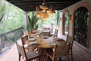 An outdoor dining area with round tables, wicker chairs, and hanging pendant lights.