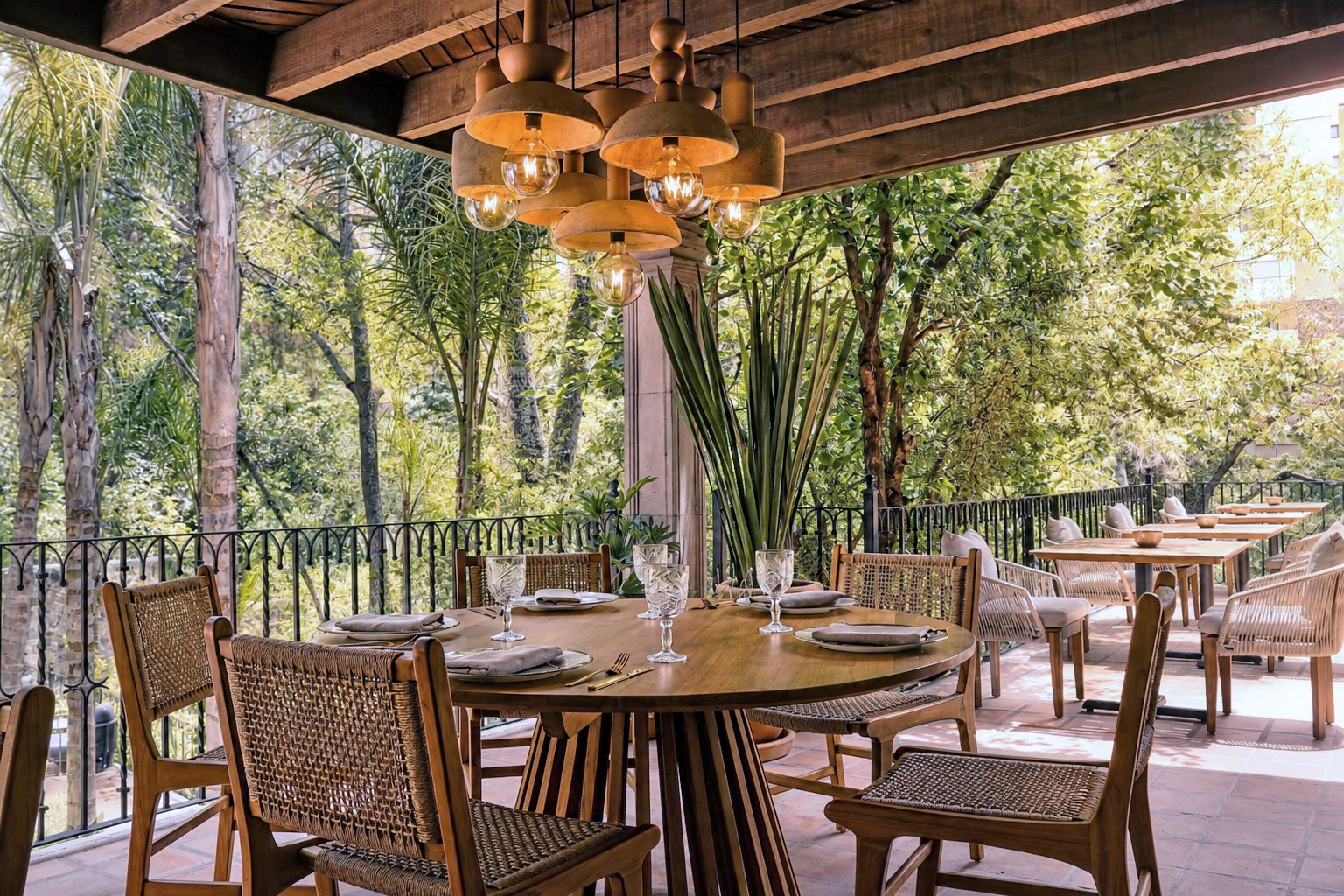 An outdoor dining area with wooden tables and chairs, surrounded by trees.