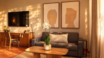 Ein Wohnzimmer mit einer Couch, einem Couchtisch, einem Fernseher und zwei gerahmten Kunstwerken an der Wand.