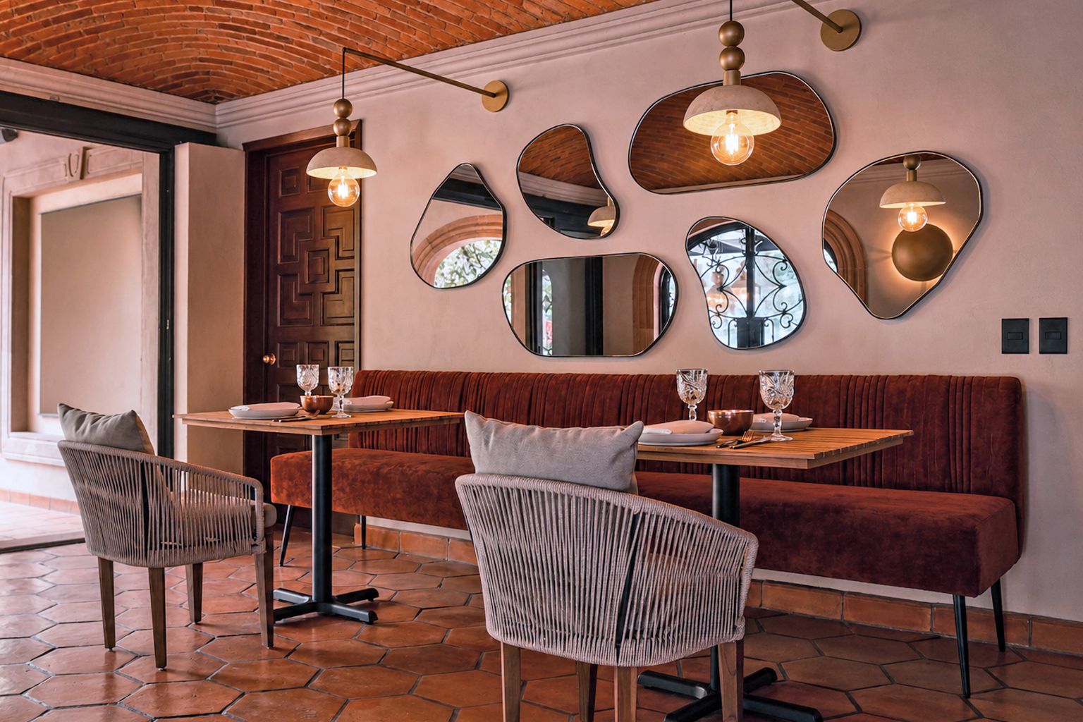 Interior de restaurante con techo de ladrillo, espejos redondos y una mesa de madera lista para comer.