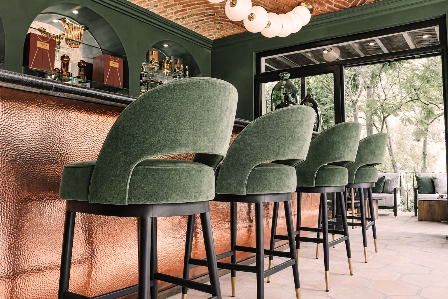 Zona de bar con taburetes tapizados en verde y una barra con textura de cobre.