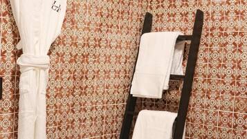 Un baño con pared de azulejos estampados, un perchero de madera y un taburete de madera con artículos de tocador.