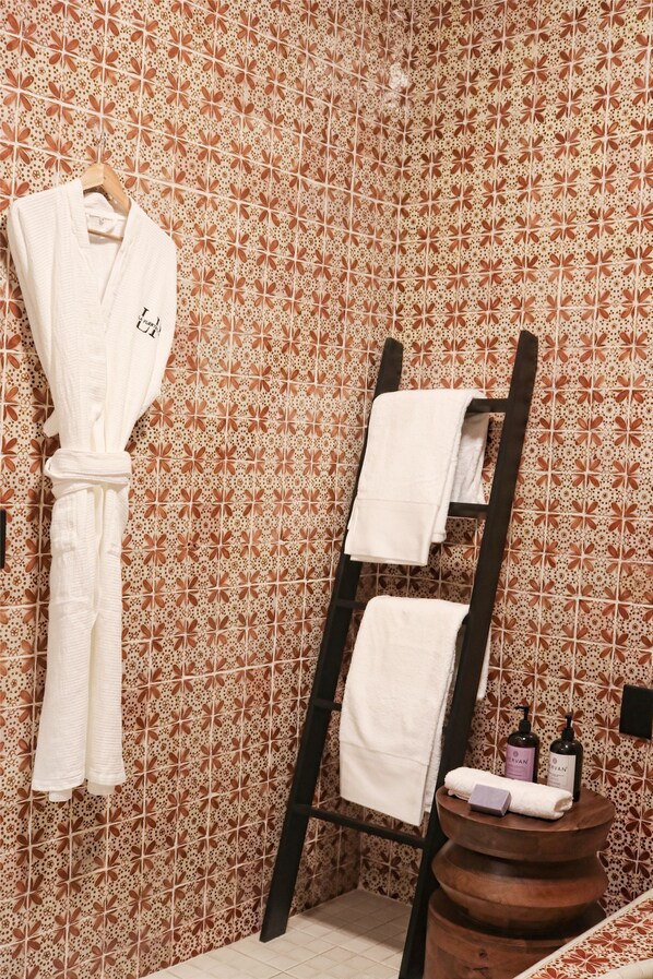 Un baño con pared de azulejos estampados, un perchero de madera y un taburete de madera con artículos de tocador.
