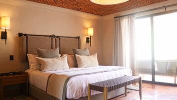 Habitación de hotel con techo de ladrillo, una cama grande con varias almohadas, una mesita de noche, un banco y vistas al exterior a través de un ventanal.