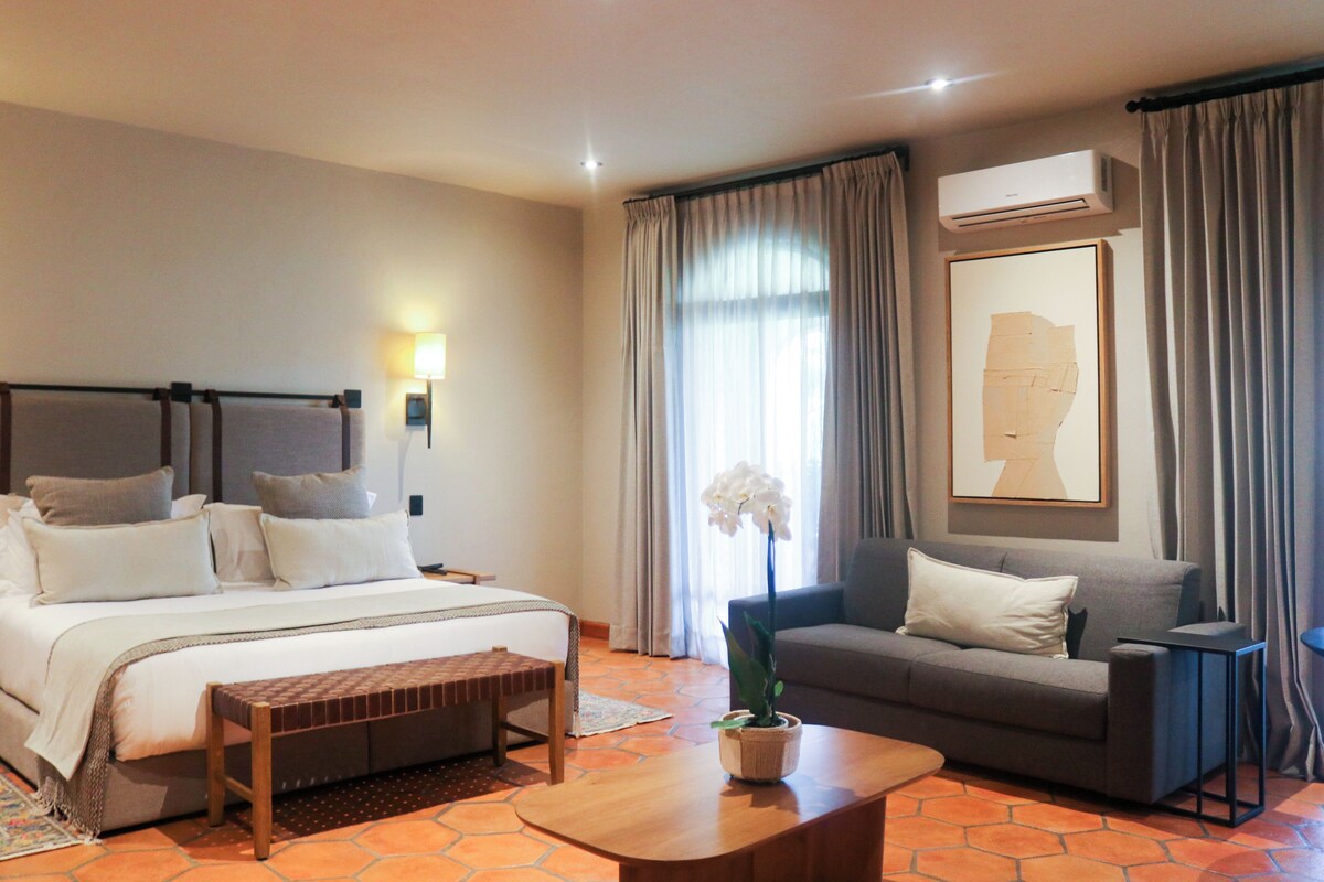 Een hotelkamer met een bed, een bank, een bijzettafeltje, een kamerplant en een schilderij aan de muur.