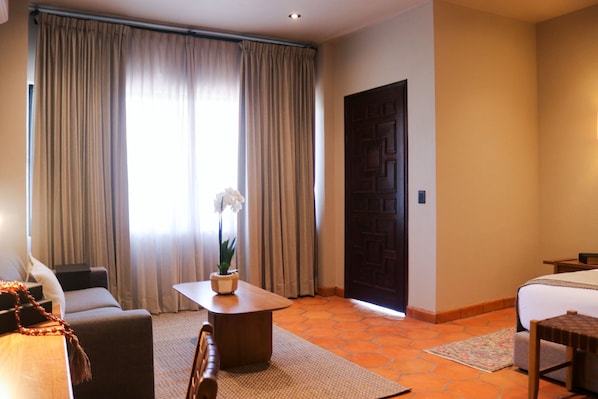 Habitación de hotel con cama, sofá, una mesita de café y una planta en maceta.