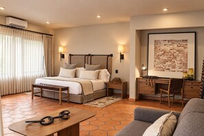 A hotel room with a bed, bedside tables, a desk with a chair, a sofa, and a large framed artwork on the wall.