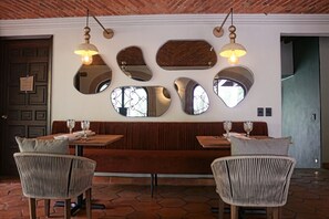 L’intérieur d’un restaurant, avec un banc en bois, des chaises en osier et un mur décoré de miroirs et de luminaires suspendus.