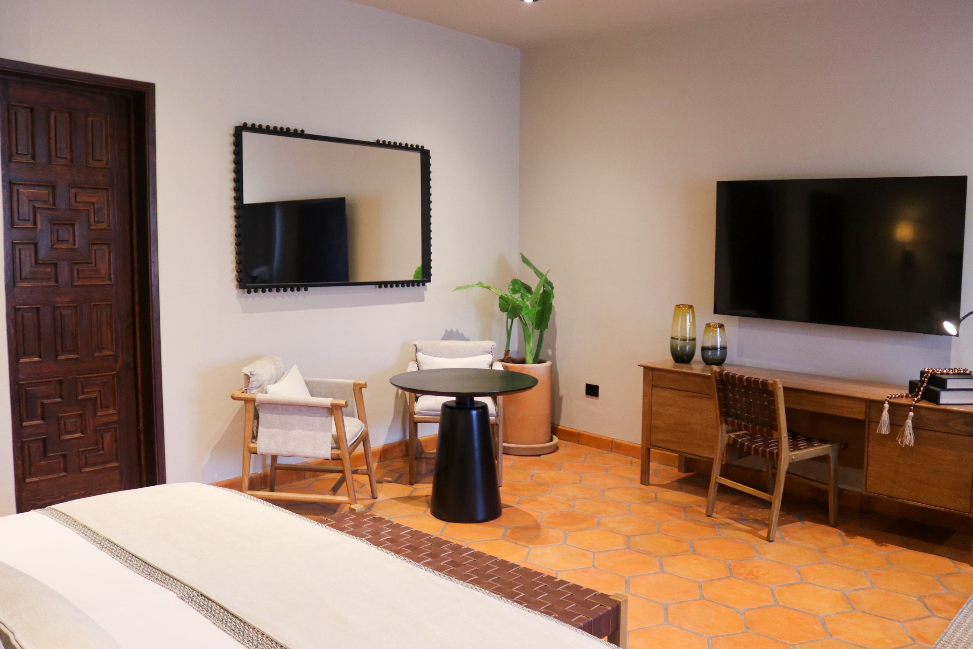 Una habitación de hotel con cama, escritorio, silla, televisor y una planta en maceta.