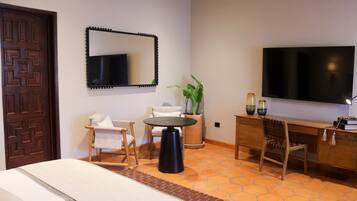 Una habitación de hotel con cama, escritorio, silla, televisor y una planta en maceta.