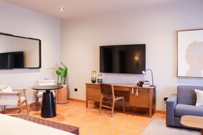 Une chambre d’hôtel moderne dotée d’une grande télévision à écran plat, d’un bureau en bois, d’un canapé confortable et d’une table à manger.
