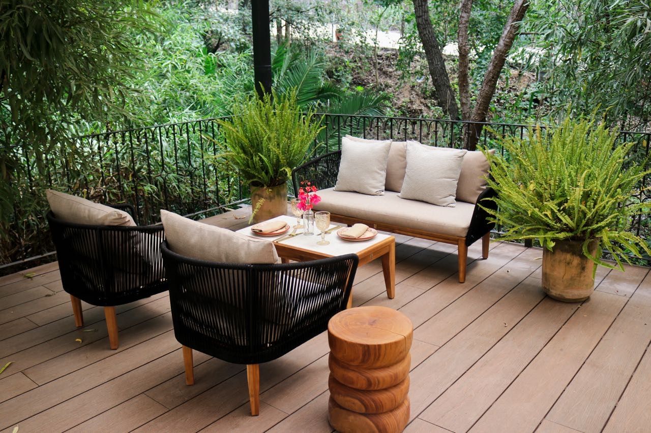 Un espacio de estar al aire libre con un sofá, dos sillones, una mesa y plantas en macetas.