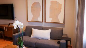 Una sala de estar con un sofá gris, una almohada blanca, una mesa de centro de madera, una orquídea en maceta y dos obras de arte enmarcadas en la pared.
