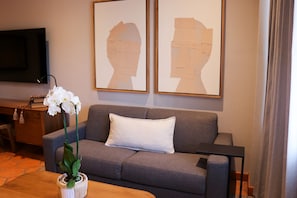 Una sala de estar con un sofá gris, una almohada blanca, una mesa de centro de madera, una orquídea en maceta y dos obras de arte enmarcadas en la pared.