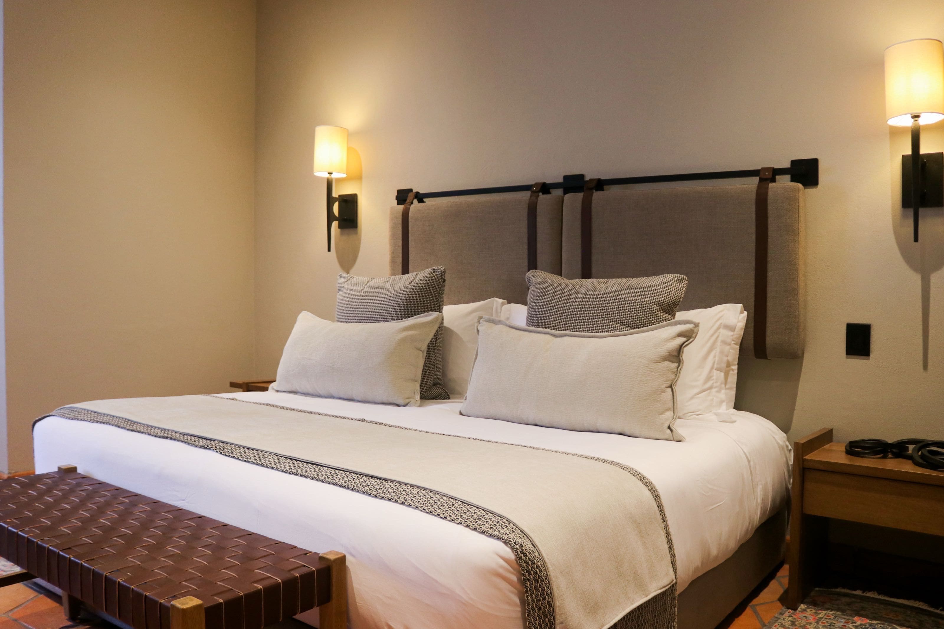 Habitación de hotel con una cama grande, dos mesitas de noche, un banco y lámparas fijadas a la pared.