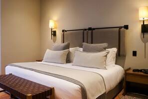 A hotel room with a large bed, two bedside tables, a bench, and wall-mounted lamps.