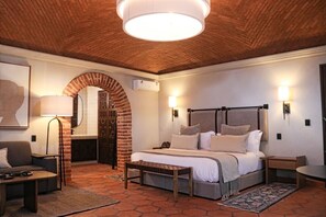 A bedroom with a brick fireplace, a bed with a headboard, a nightstand, a lamp, and a wall-mounted light fixture.