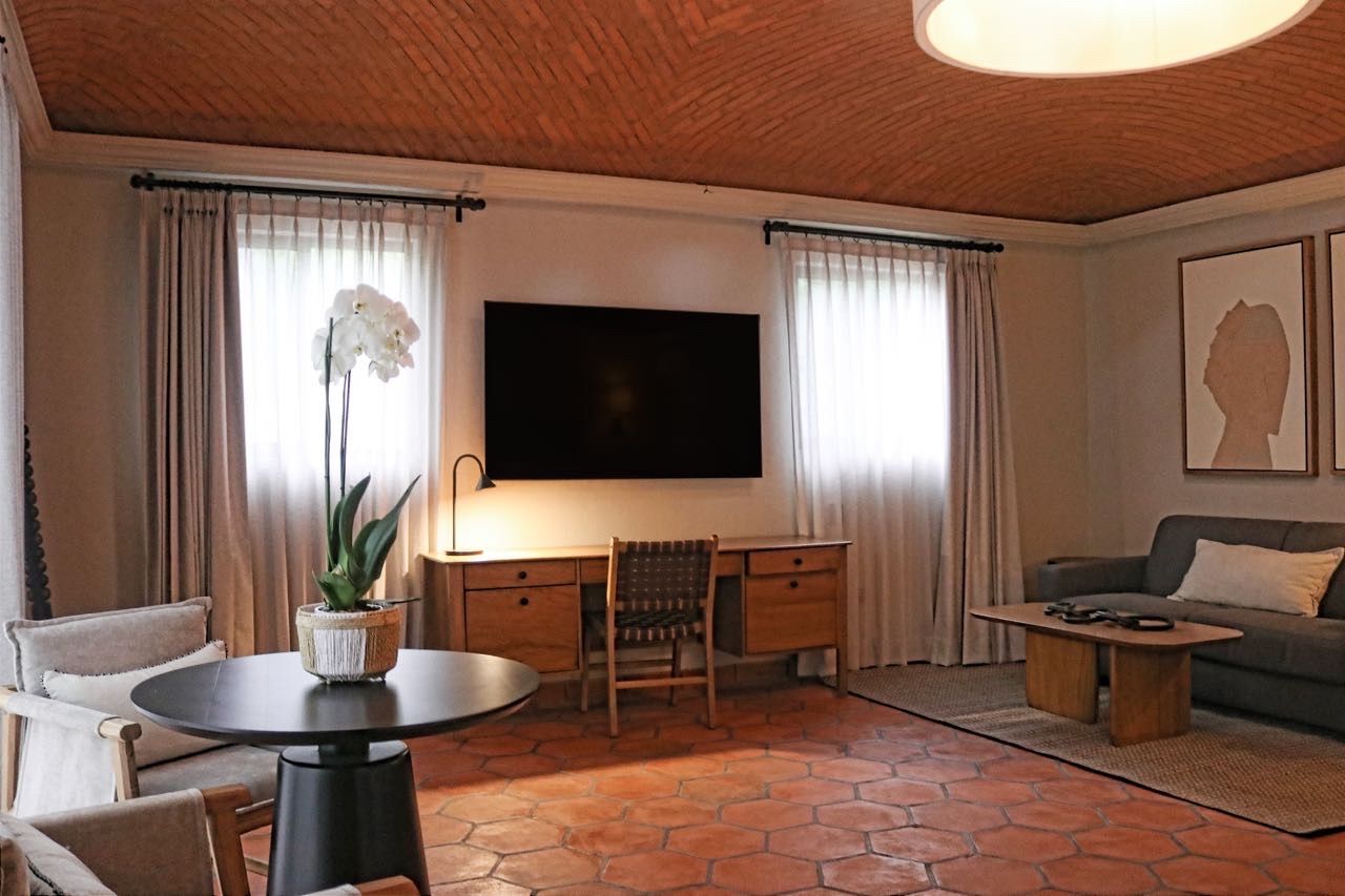 Una sala de estar con una televisión de pantalla plana, un escritorio, una silla, un sofá y una mesa de centro.